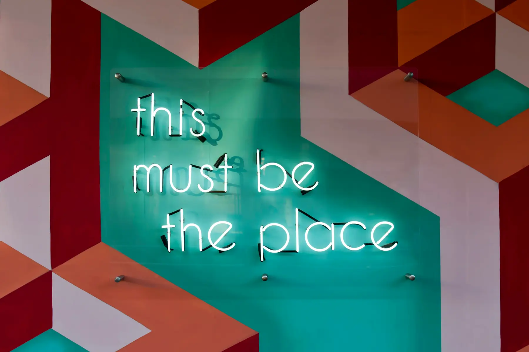 Enseigne néon « this must be the place » sur un mur graphique coloré, symbole d'une marque employeur qui donne envie de rejoindre l'entreprise